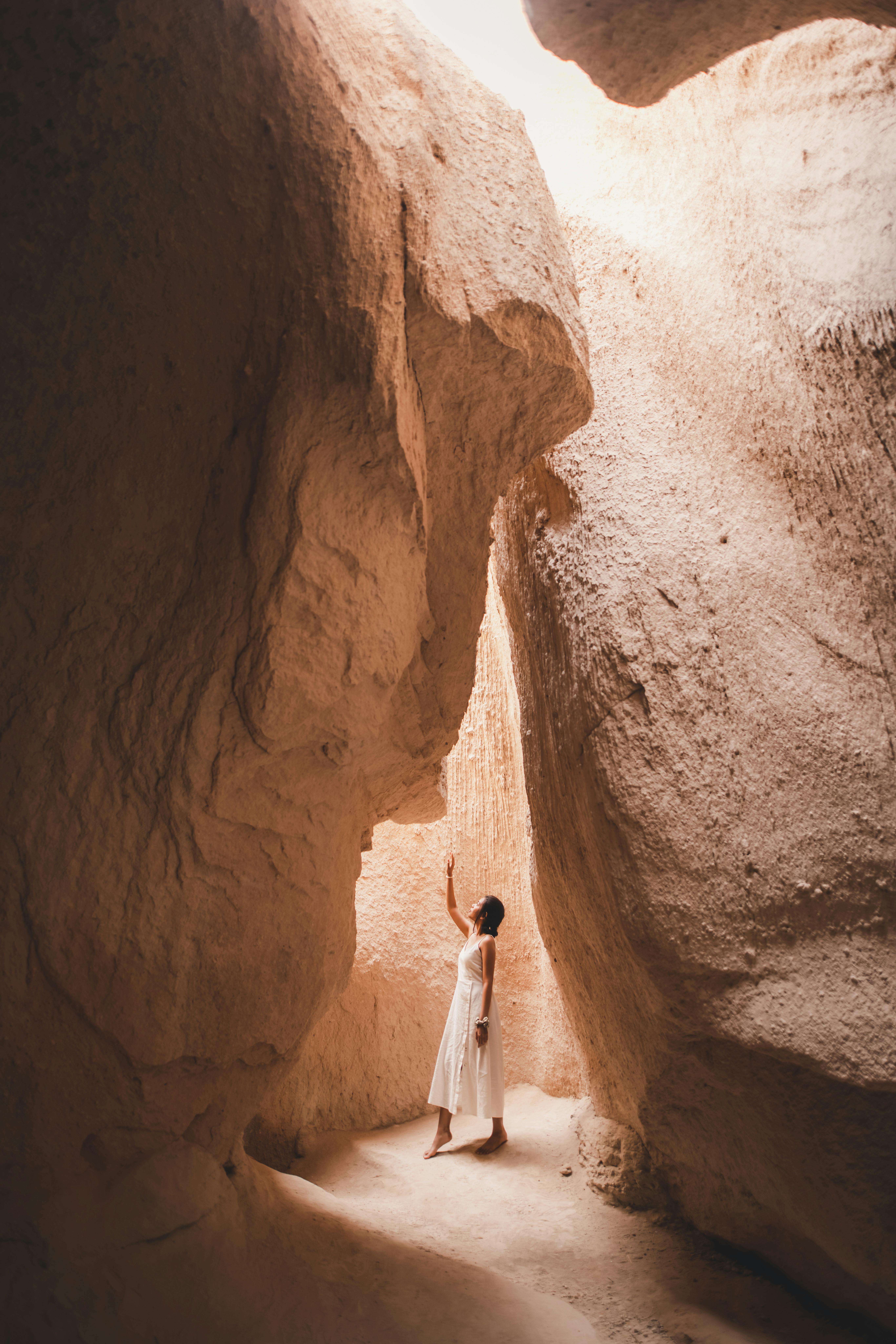 A woman in white dress stands in Göreme, Türkiye's rocky canyon, reaching upwards.