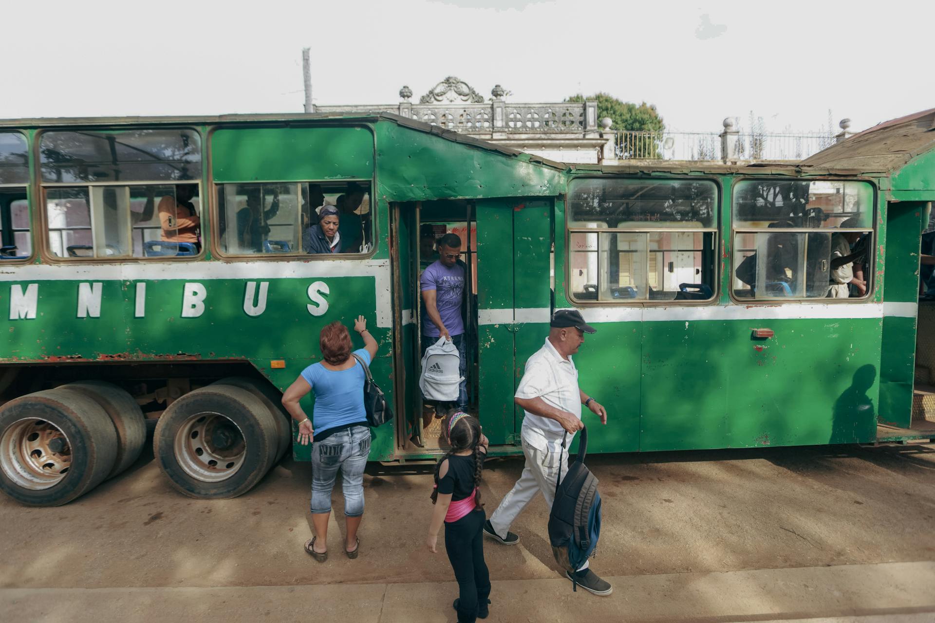 A family and other passengers board a vintage green bus on a sunny day, capturing everyday public transport.