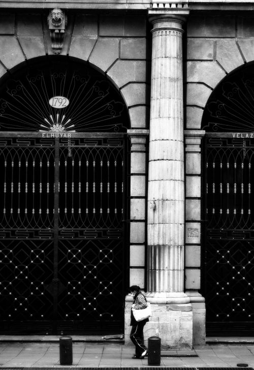 Free Black and white street photo of a woman walking by ornate iron gates in Ciudad de México, CDMX. Stock Photo
