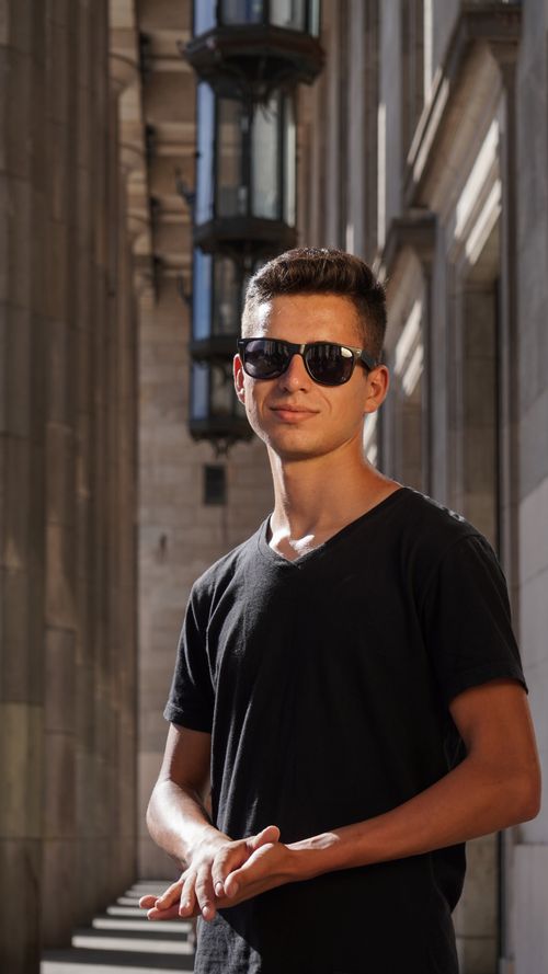 Free A young man wearing sunglasses smiles confidently in an urban setting, capturing the essence of summer. Stock Photo