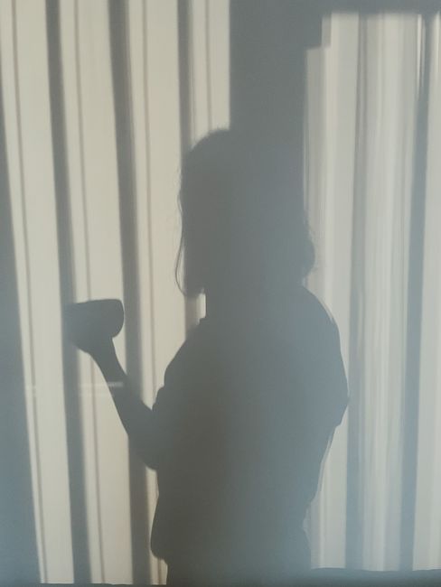 Moody silhouette of a person holding a mug, cast on curtains in Istanbul.