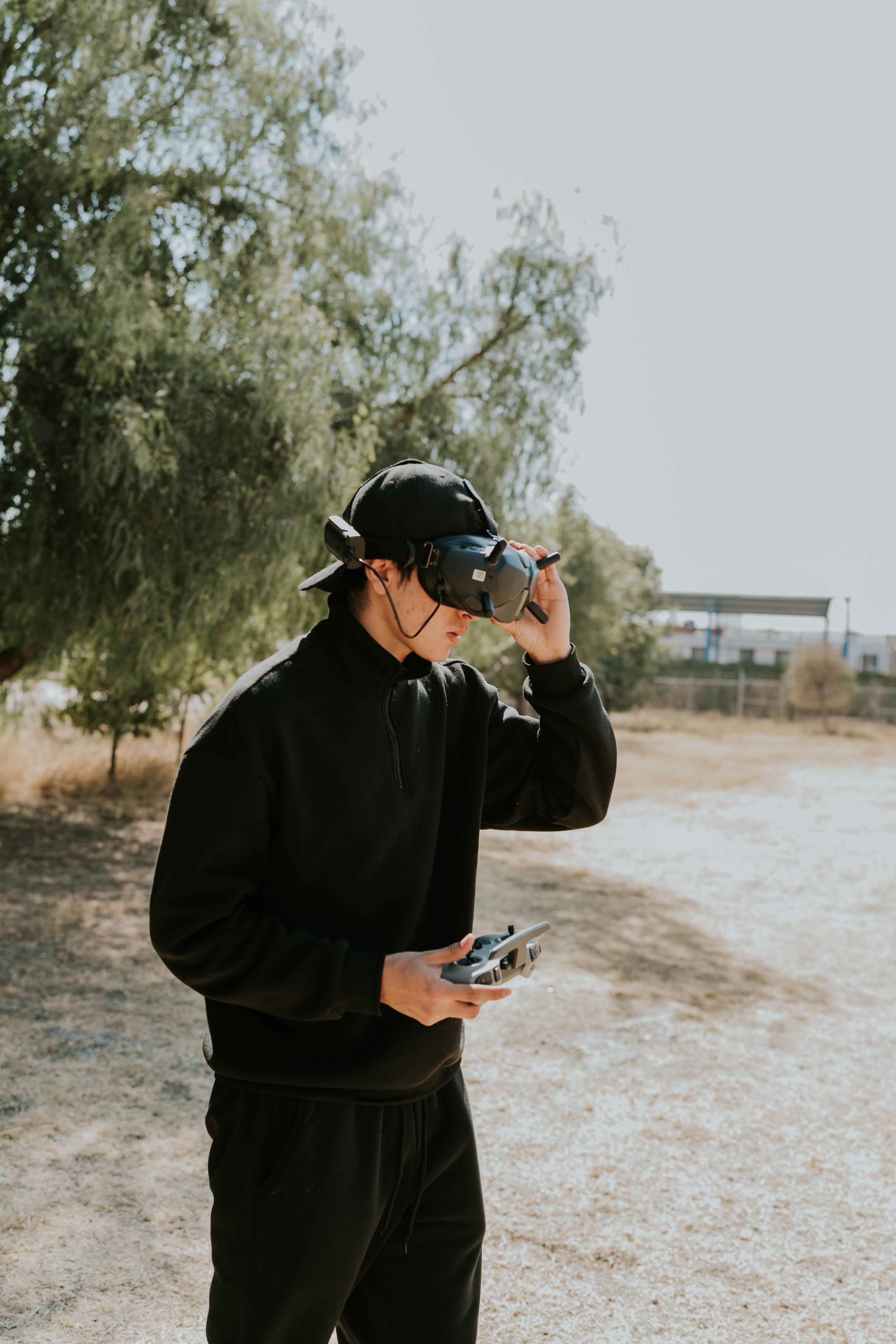 Young man using drone and VR goggles in sunny outdoor setting.