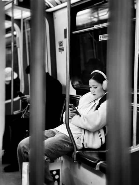 A woman with headphones sits quietly on a metro train, engaged with her smartphone.