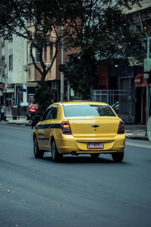 Free Rear view of a yellow taxi driving on an urban street, showcasing city transportation. Stock Photo