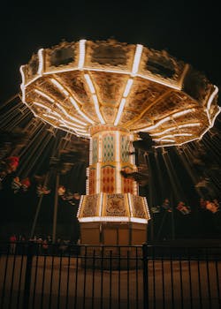 A vibrant nighttime photograph of an illuminated chair swing ride with people, captured with motion blur.