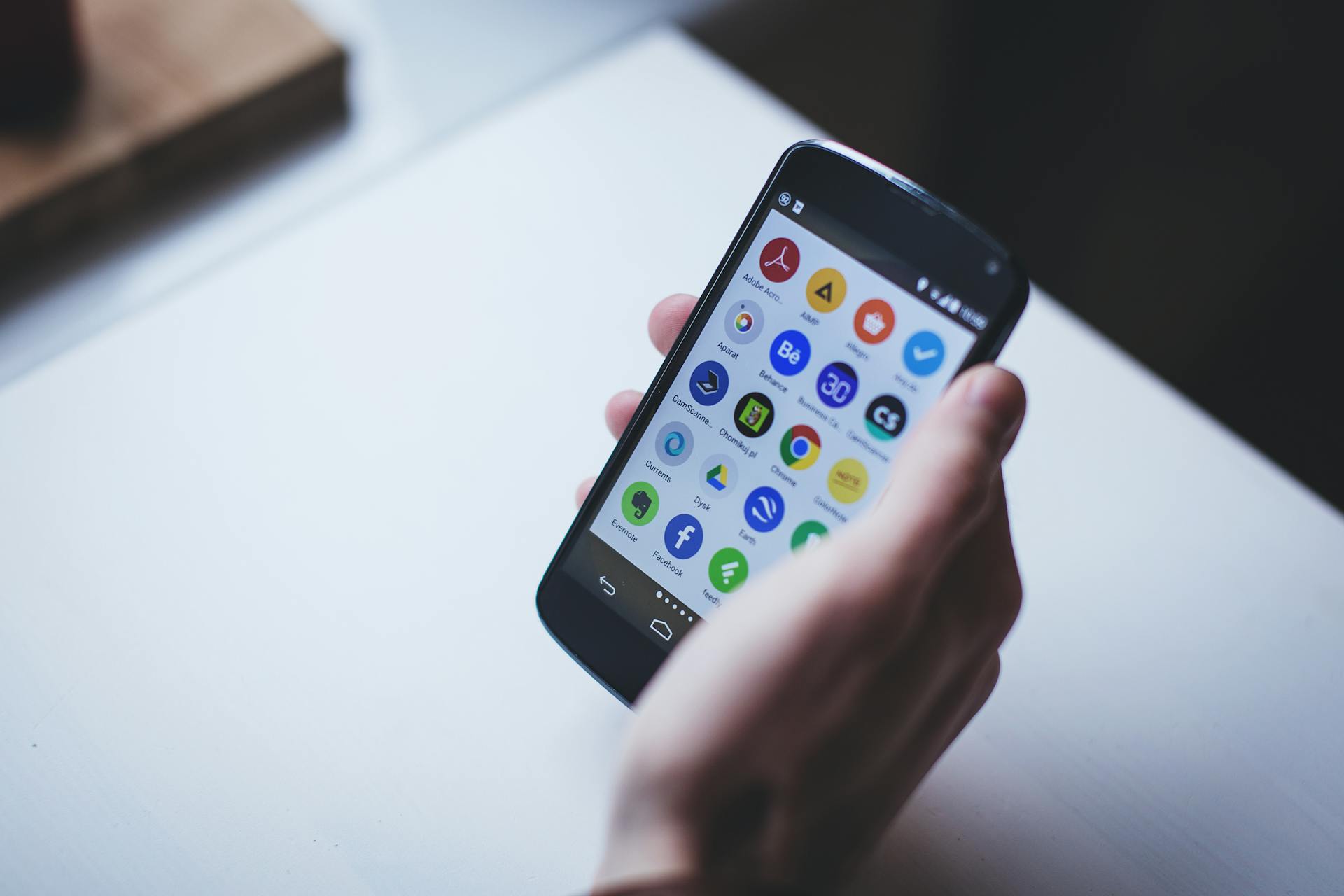 Close-up of a person holding a smartphone with various app icons visible on the screen.