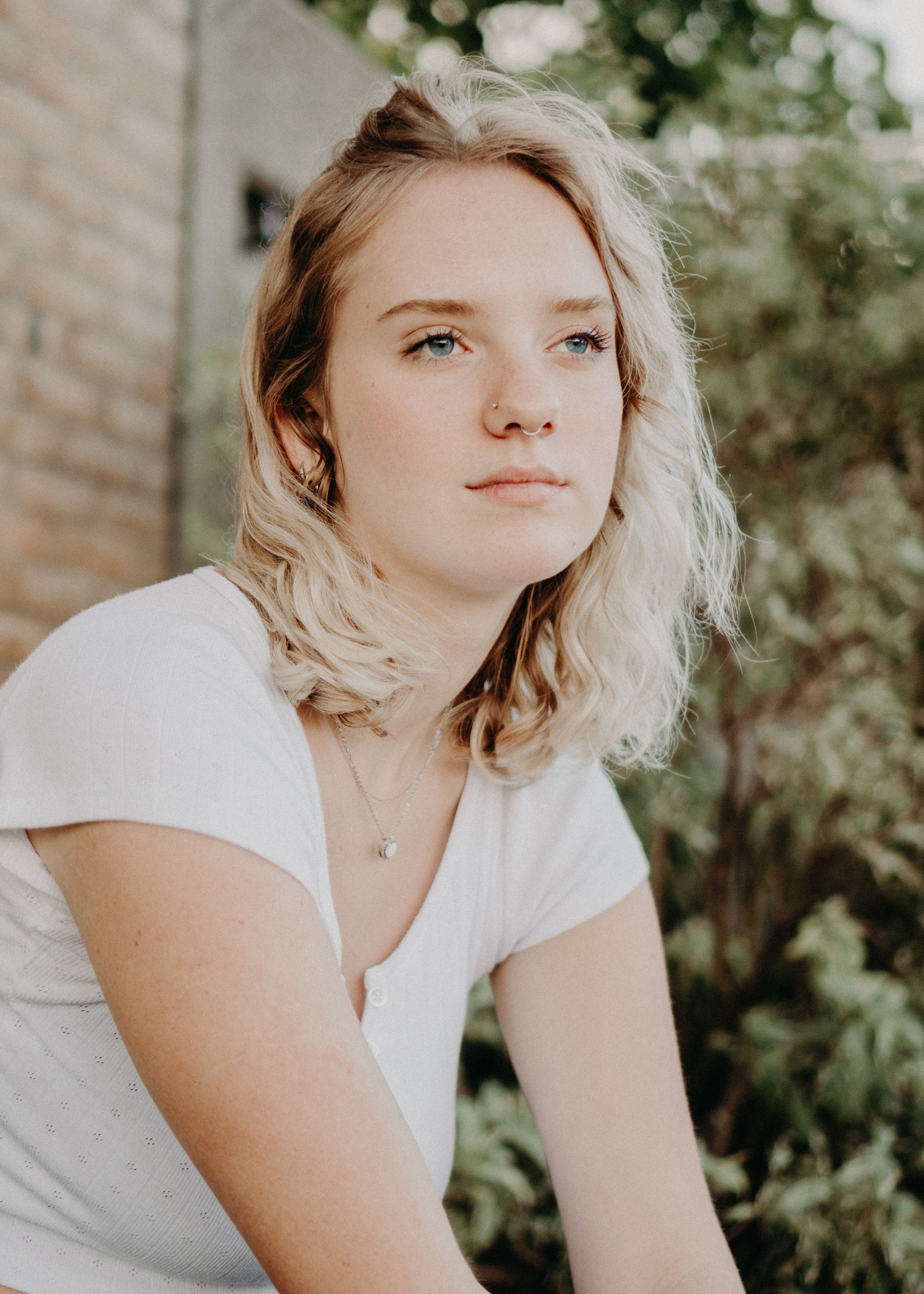 A serene portrait of a young woman with blonde hair sitting outdoors in natural lighting.