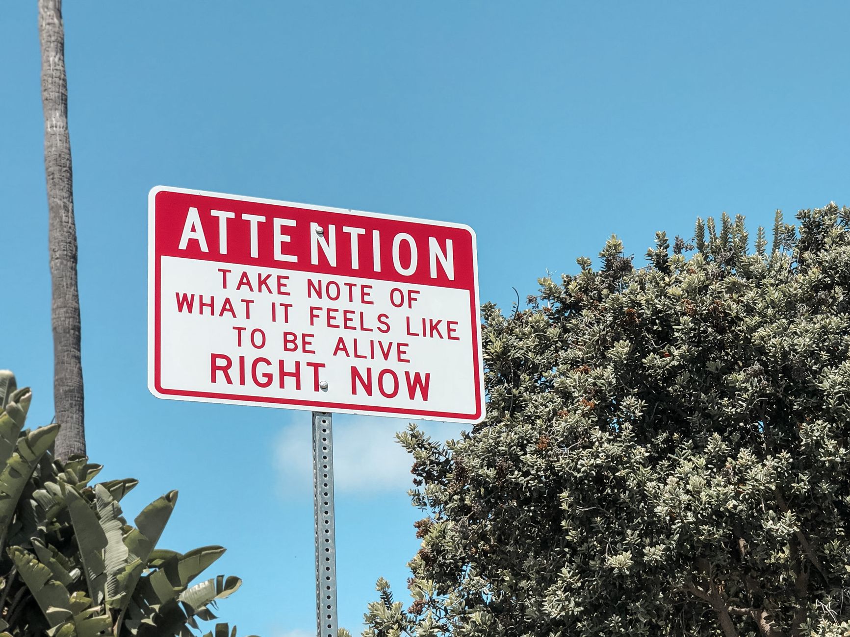 Motivational street sign against a bright blue sky in Laguna Beach, California.