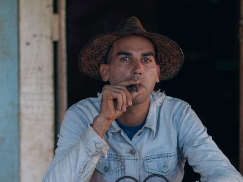 Free A man wearing a wide-brimmed hat smokes a cigar, displaying a contemplative expression. Stock Photo