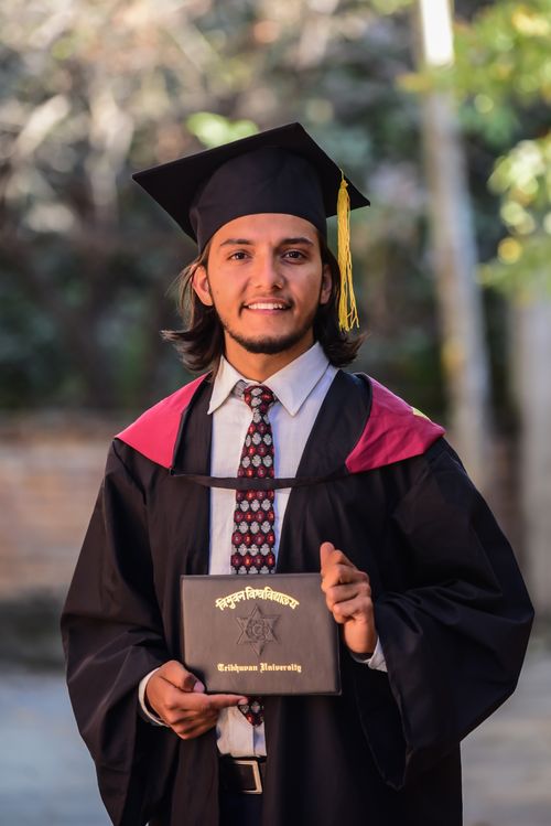 Free Proud graduate in cap and gown holding diploma outdoors, celebrating academic success. Stock Photo