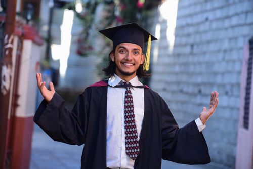 Free Smiling graduate celebrating success outdoors in academic regalia. Stock Photo