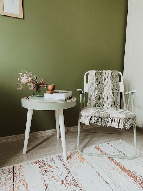 A Chair and Small Table with a Dried Bouquet Standing next to a Green Wall 