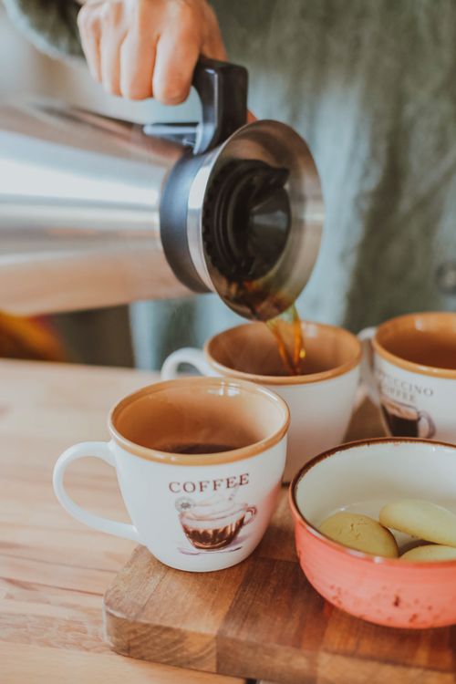 Free Close-up of coffee being poured into mug with biscuits nearby in a cozy setting. Stock Photo