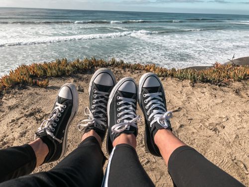 Free Two people relaxing on Carlsbad beach wearing matching sneakers during a sunny day. Stock Photo