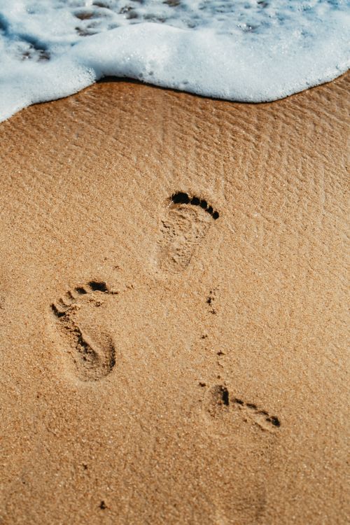 Free Close-up of footprints in sand near ocean waves at the beach. Stock Photo