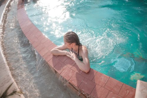 Free A woman enjoys a sunny day at the pool, leaning on the edge with tranquil waters. Stock Photo