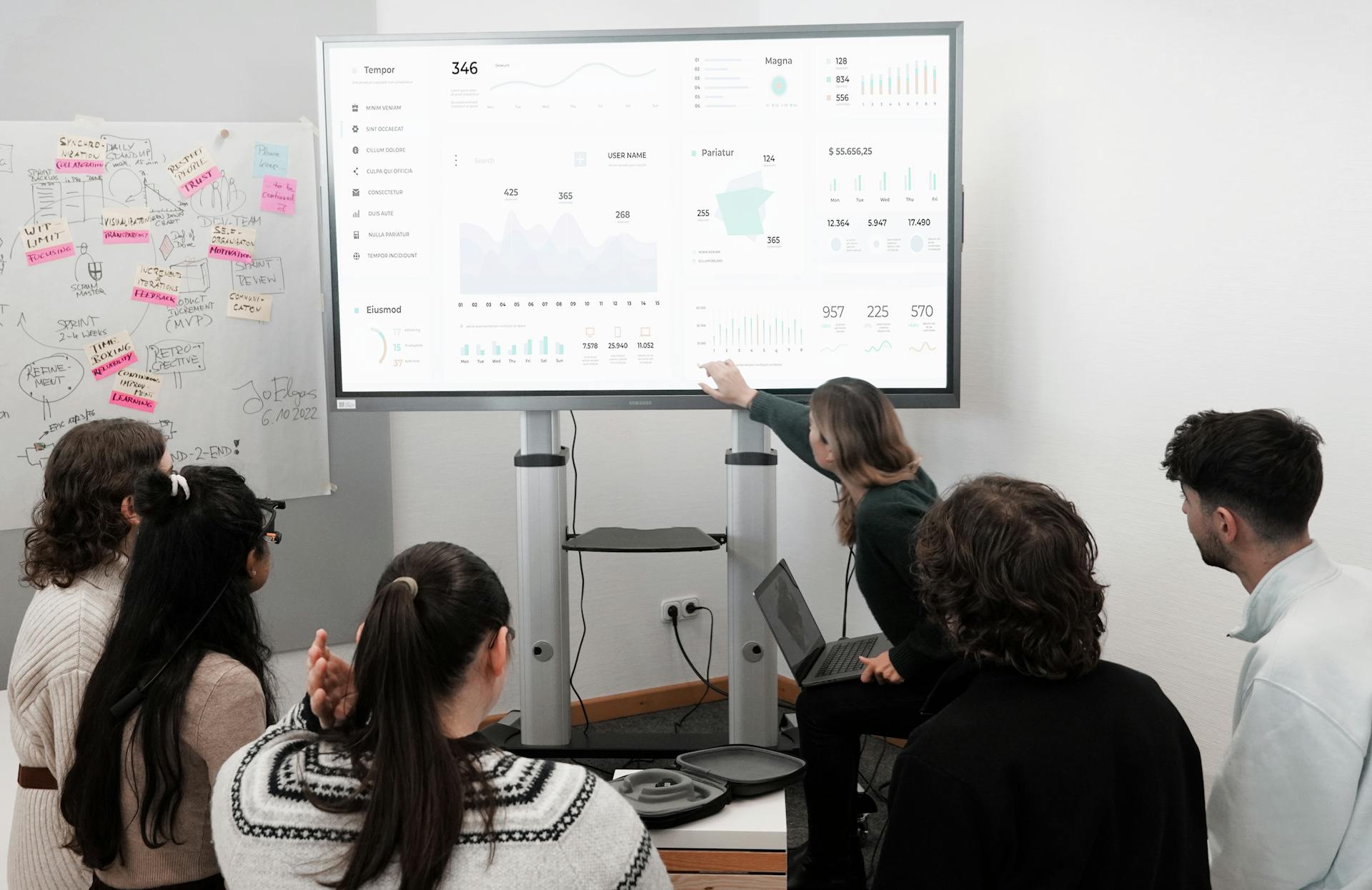 Group of professionals engaged in a business presentation examining charts on a large screen.