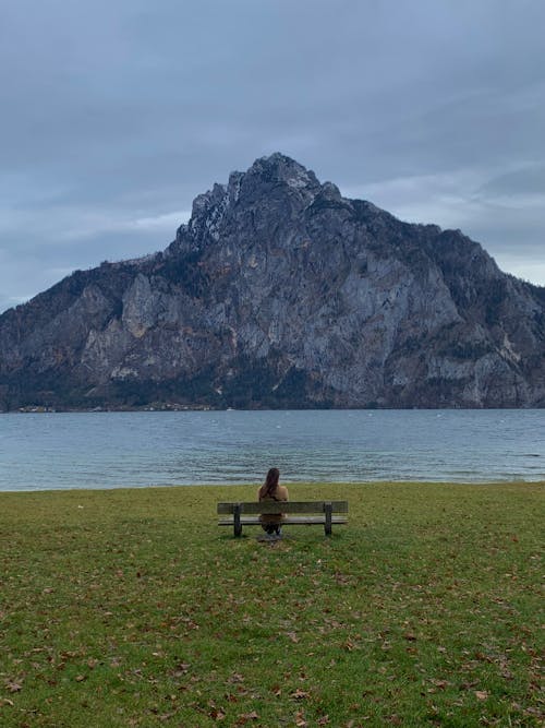 Free Woman Sitting on a Bench and Looking at a View of Mountain and Lake  Stock Photo