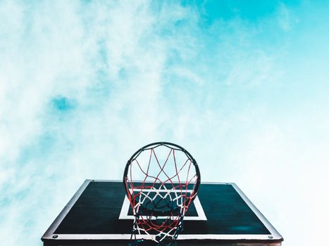 A striking low angle shot of a basketball hoop with a clear blue sky backdrop, capturing the essence of outdoor sports.