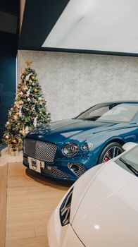 A luxury car showroom featuring elegant cars beside a beautifully decorated Christmas tree.