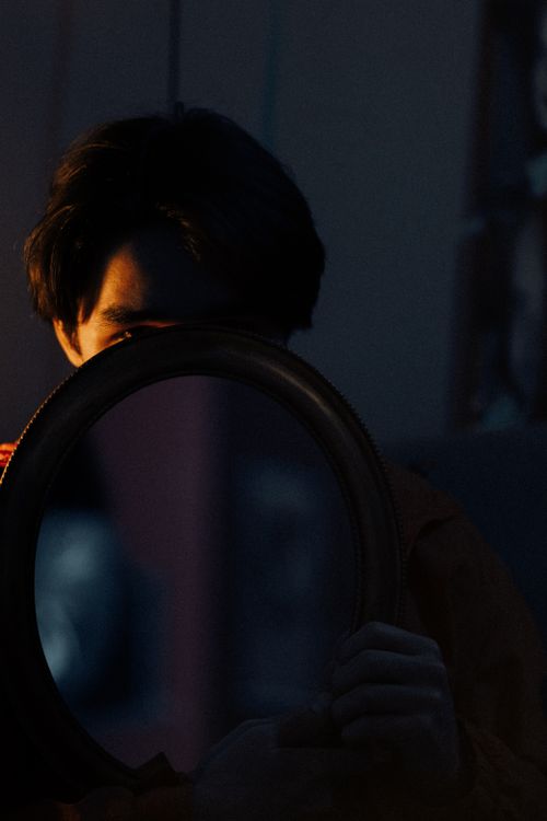 Free A mysterious portrait featuring a person holding a mirror, partially obscuring their face, in low light. Stock Photo