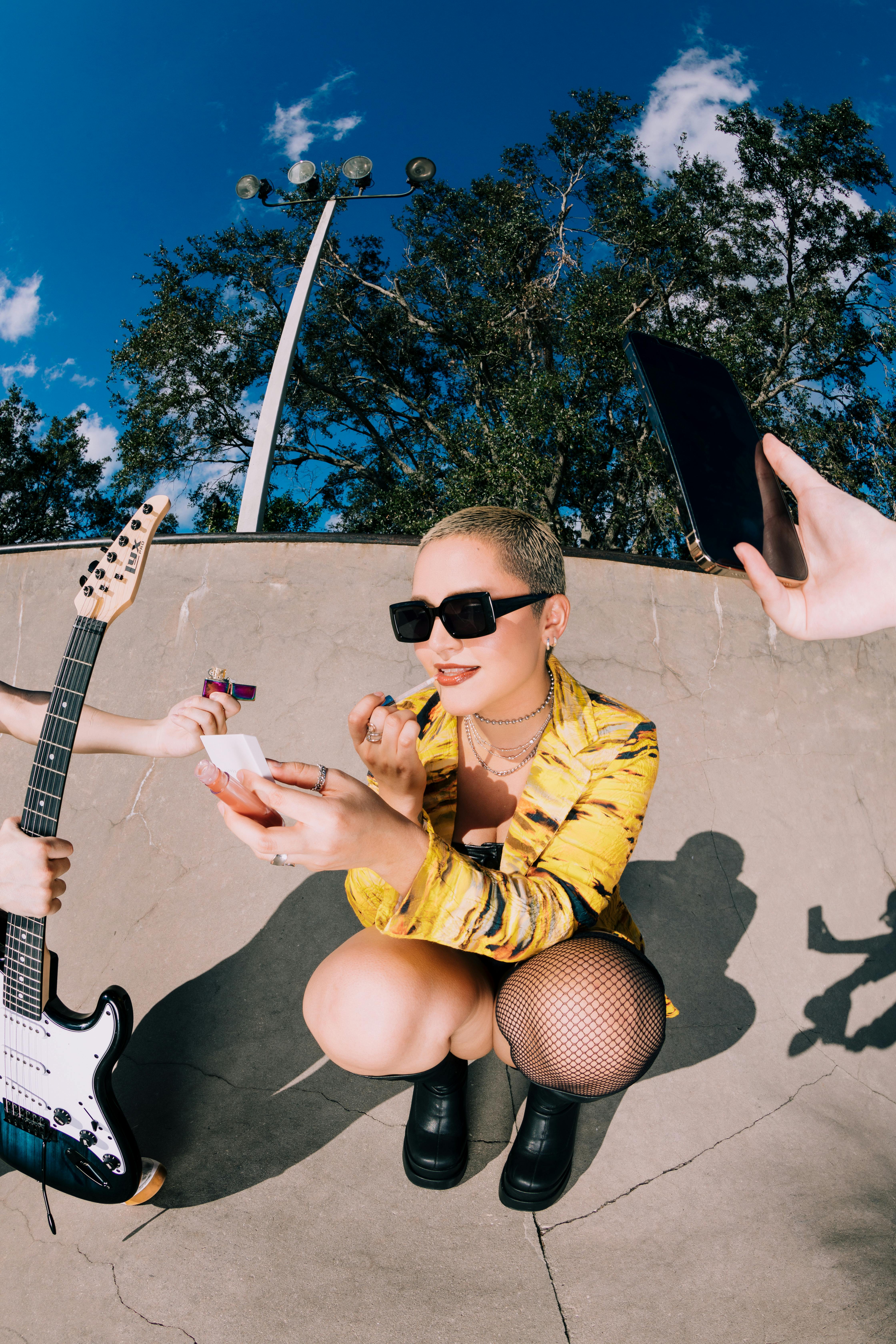 Stylish woman at a skatepark putting on makeup, capturing a vibrant outdoor scene.