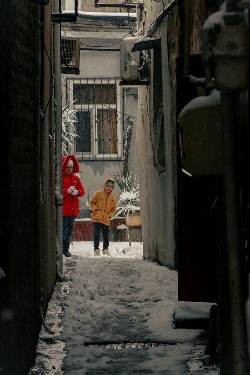 Free Two kids in winter coats walking through a snowy alleyway in a city. Stock Photo