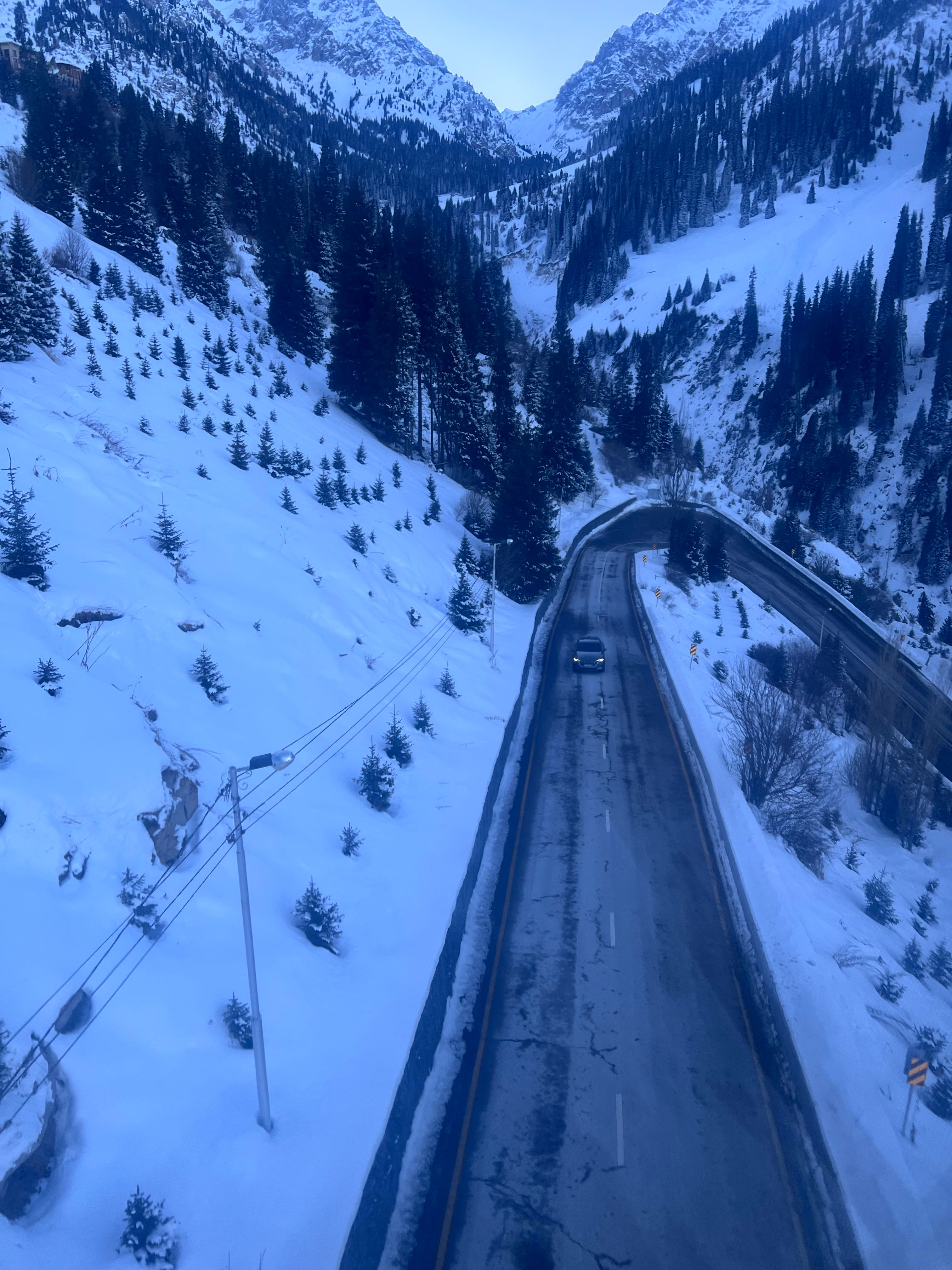 Aerial view of a winter road through snowy mountains and pine forests.