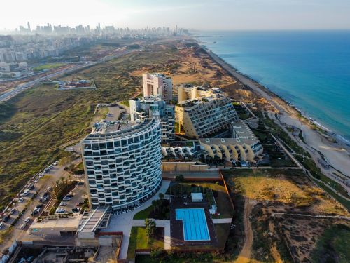 Free Drone shot capturing a cityscape and coastline, featuring modern architecture and blue sea under a clear sky. Stock Photo