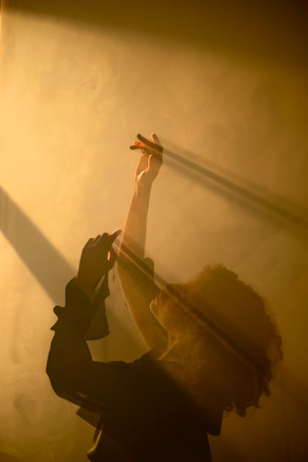 A woman in silhouette dances gracefully, enveloped in warm light and shadows, creating an artistic scene.