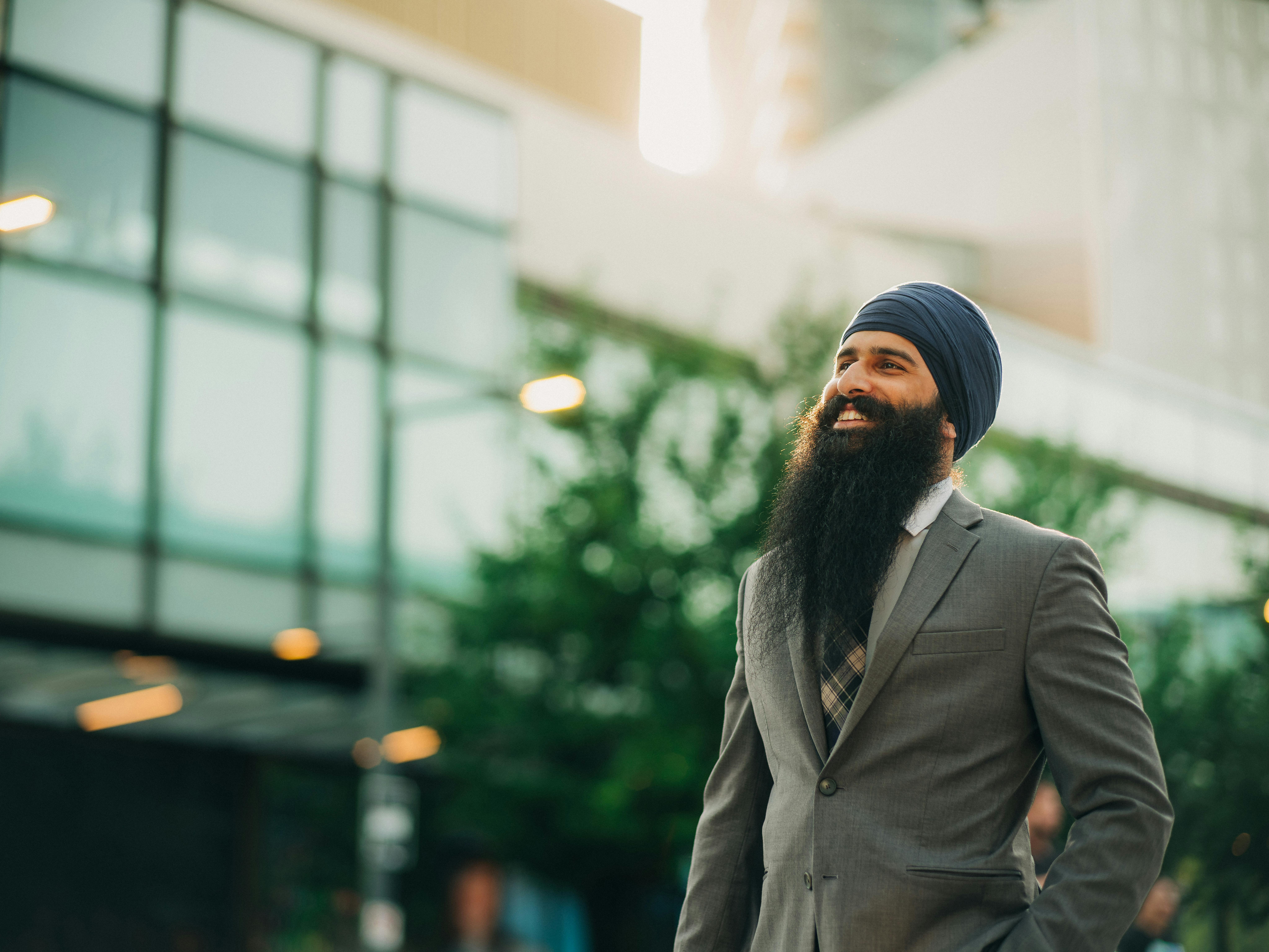 Smiling man in business attire with turban outdoors, exuding confidence and positivity.