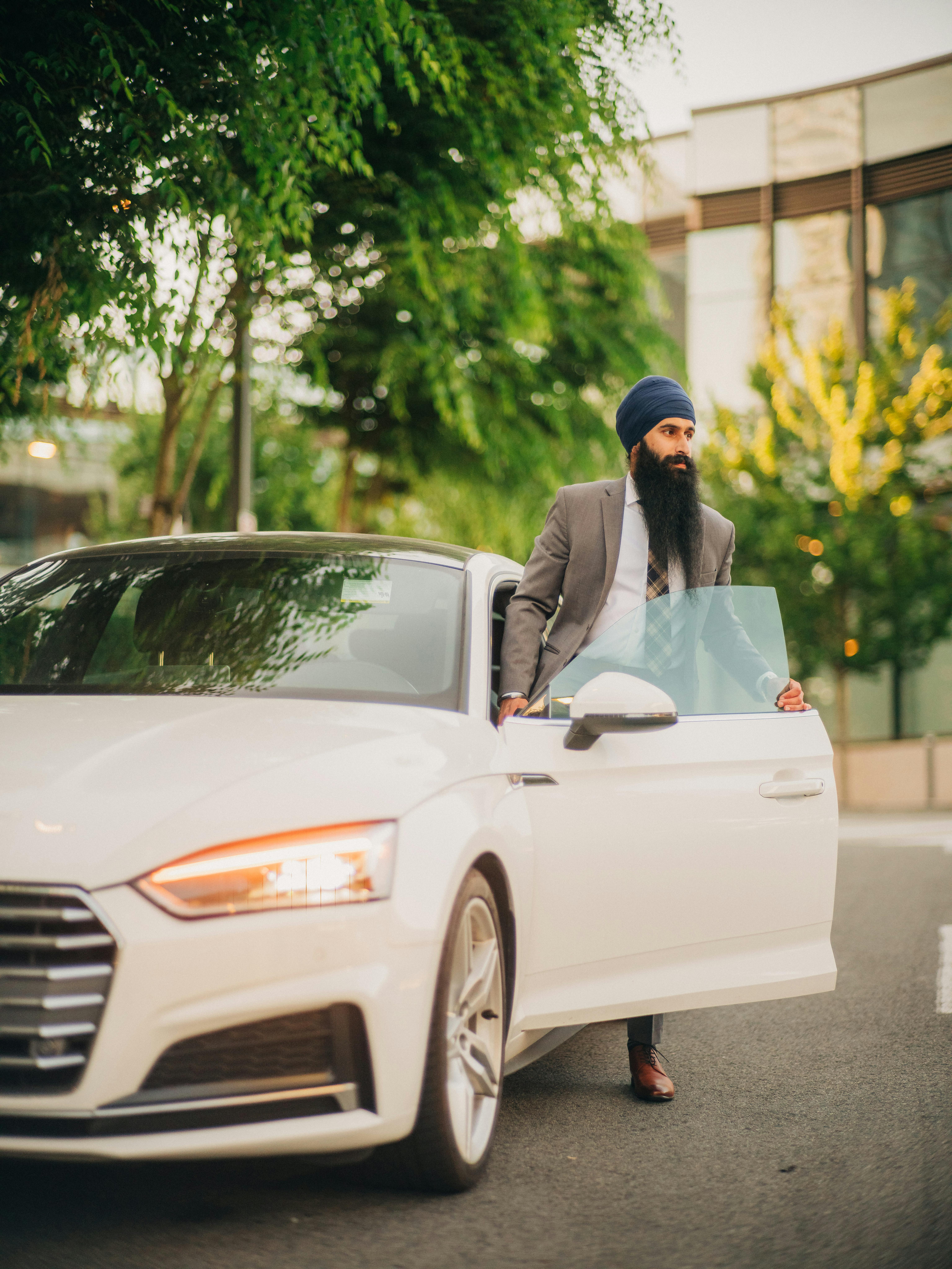 Free Man wearing a turban stepping out of a luxury white car in an urban setting. Stock Photo