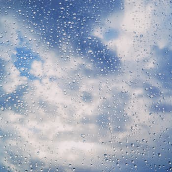 Close-up of raindrops on a window pane against a cloudy blue sky.