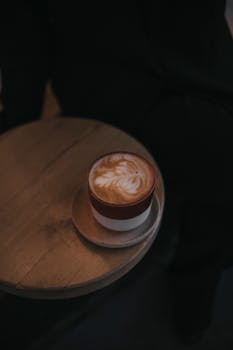 A beautifully crafted frothy coffee sits on a rustic wooden table, showcasing intricate latte art.