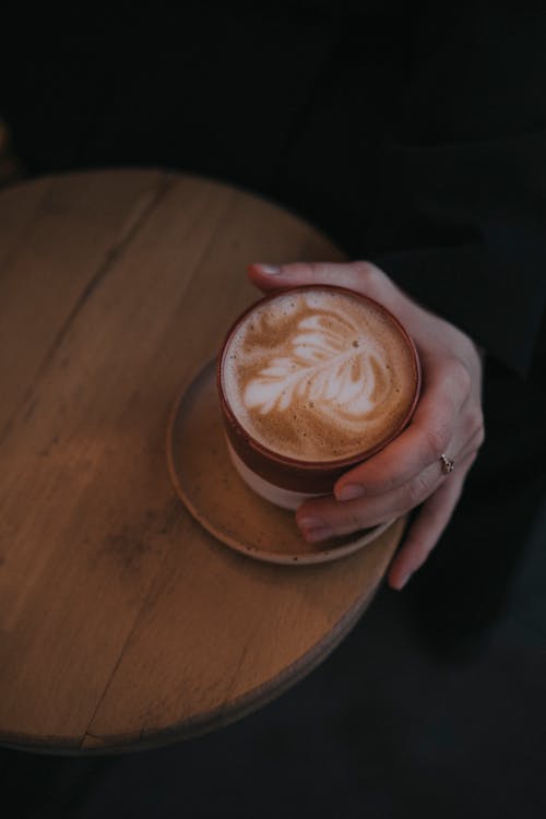 Close-up of Woman Hand with Coffee on Wooden Table