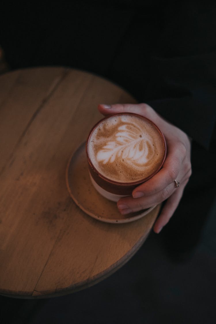 Close-up Of Woman Hand With Coffee On Wooden Table