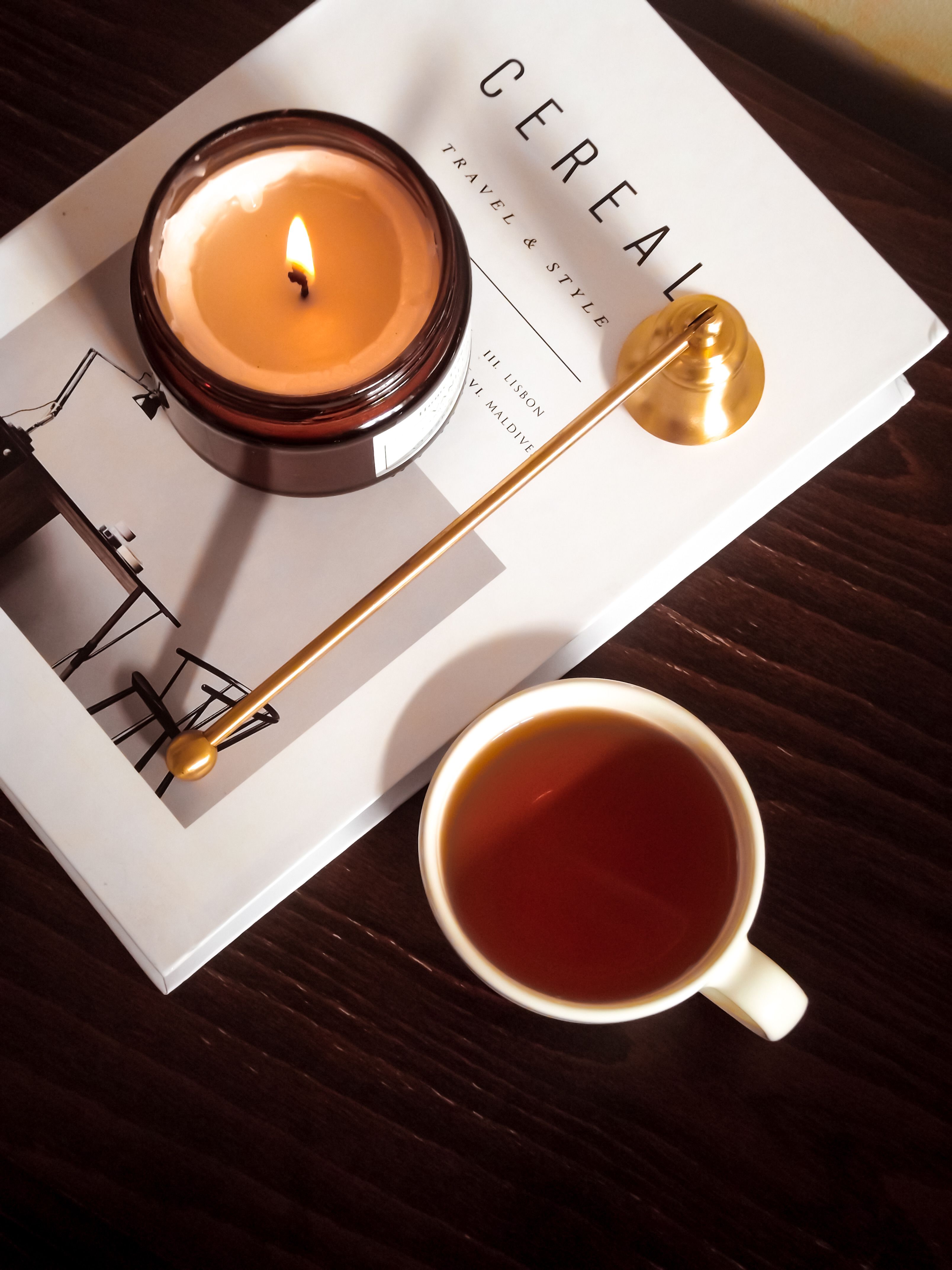 Warm and inviting scene with a candle, tea cup, and a style book on a wooden surface.