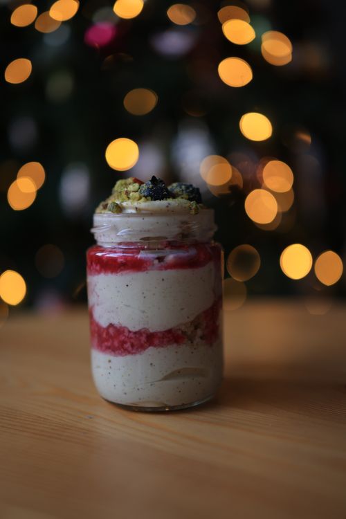 Free Delicious yogurt dessert with berries and nuts in a jar, set against festive bokeh lights. Stock Photo