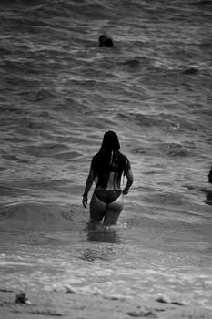 Black and white photo of woman entering ocean, viewed from behind.