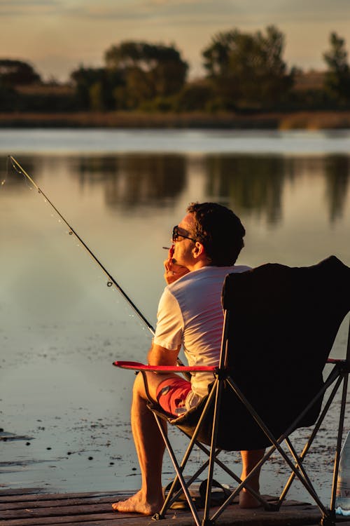 Man Holding Fishing Rod While Sitting on Camping Chair