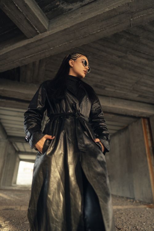 Free Fashionable woman in a black leather coat posing under an urban structure, exuding confidence and style. Stock Photo