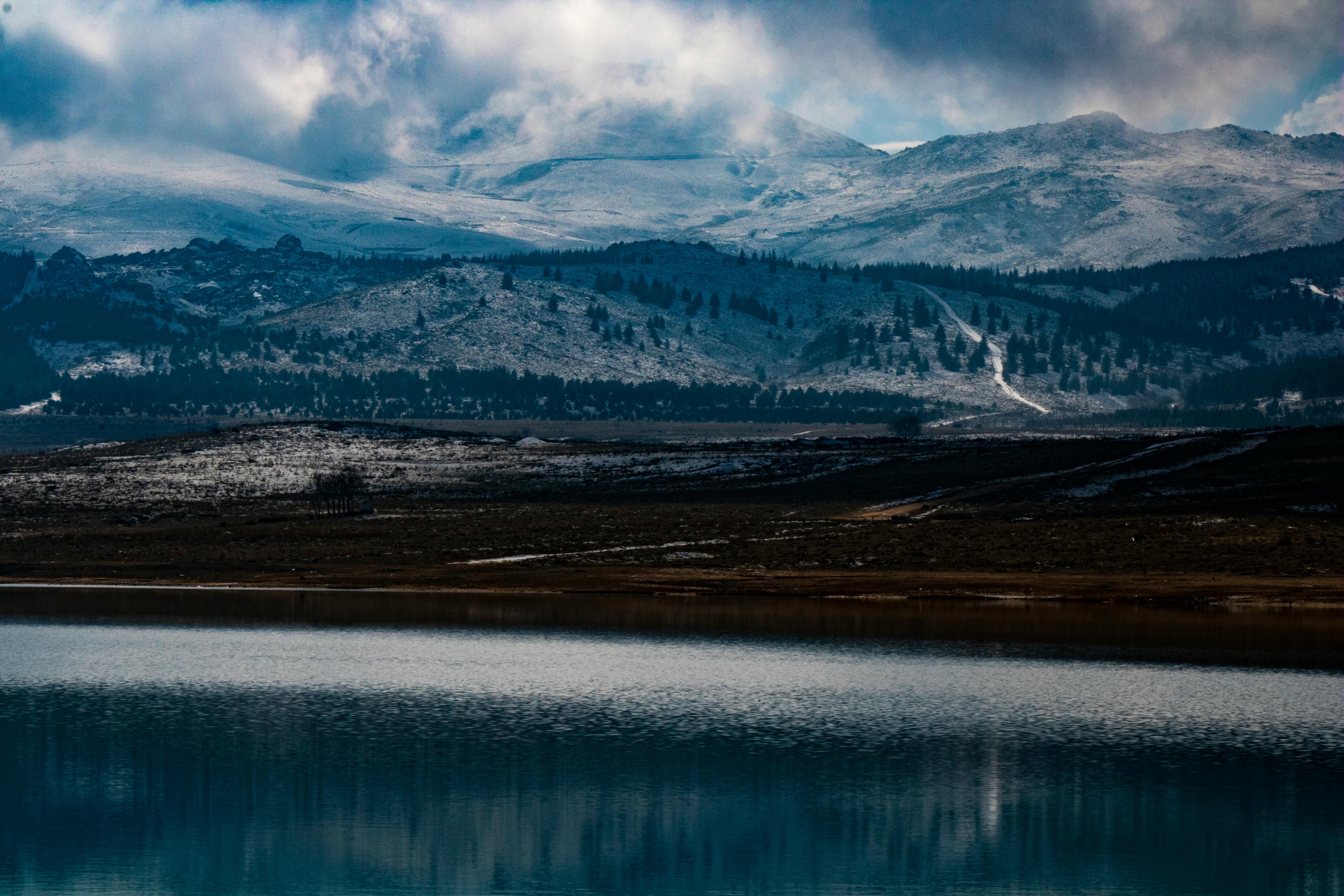 Serene winter mountains reflected in calm lake beneath dramatic sky.