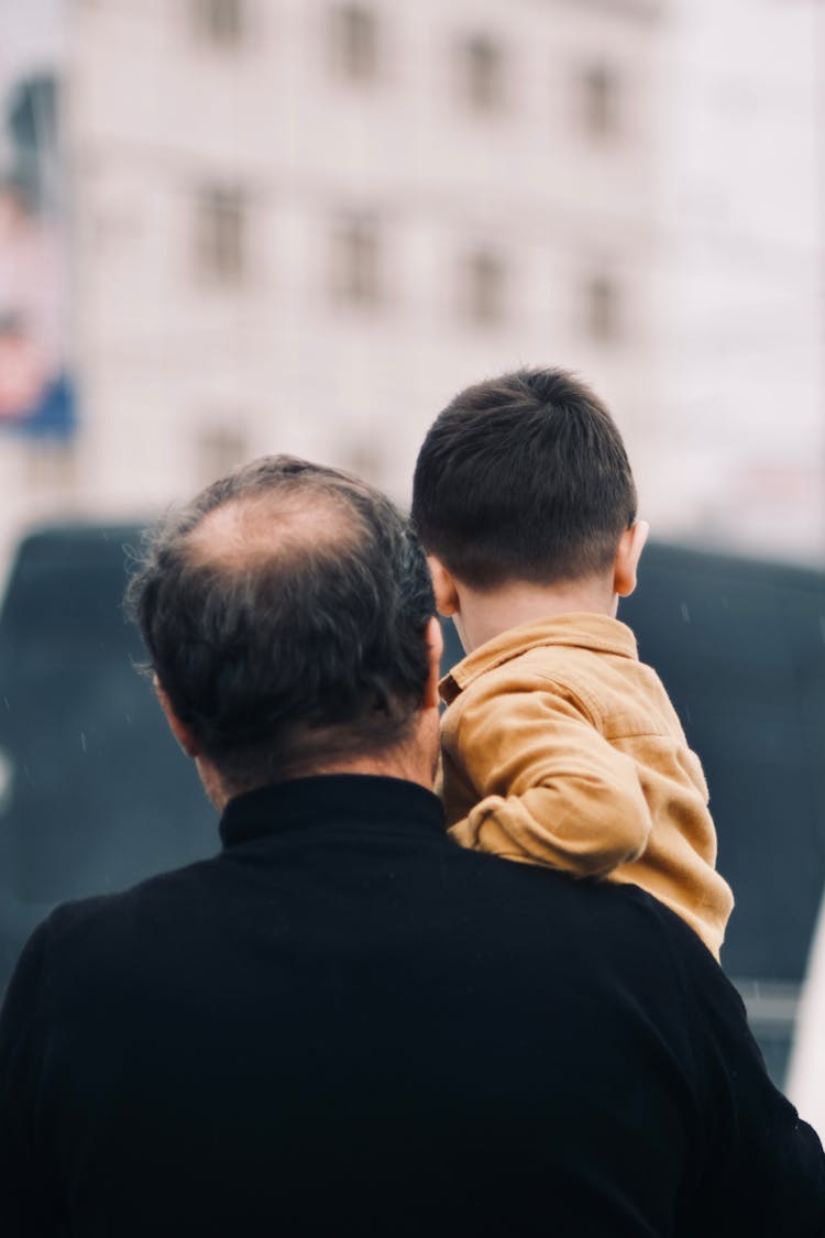 Back View Of A Father Carrying His Son