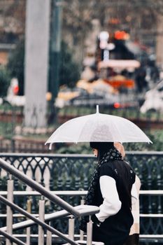 City scene with woman using umbrella, highlighting rainy day fashion.