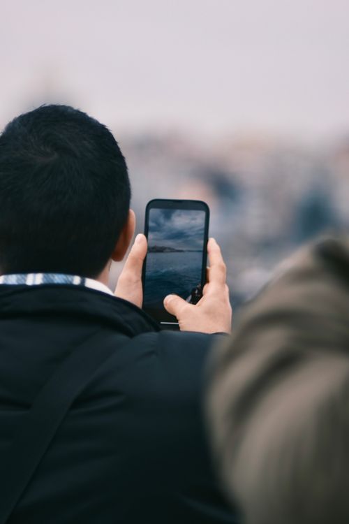 Free Back view of person taking a photo with a smartphone outdoors. Stock Photo