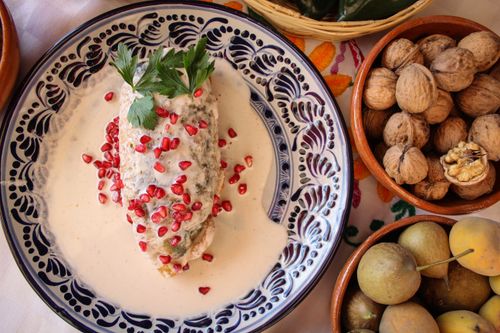 Free Traditional Mexican dish Chile en Nogada with pomegranate, nuts, and fruits, beautifully presented on a decorative plate. Stock Photo