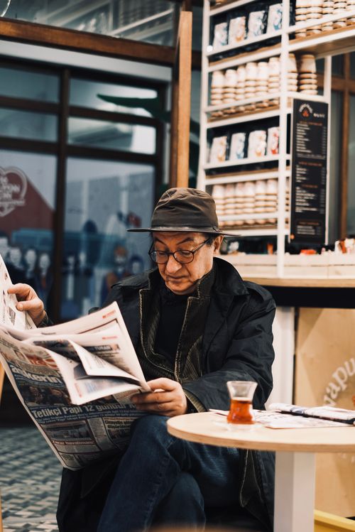 Free Man in casual attire reads a newspaper at a café, enjoying a relaxing moment. Stock Photo