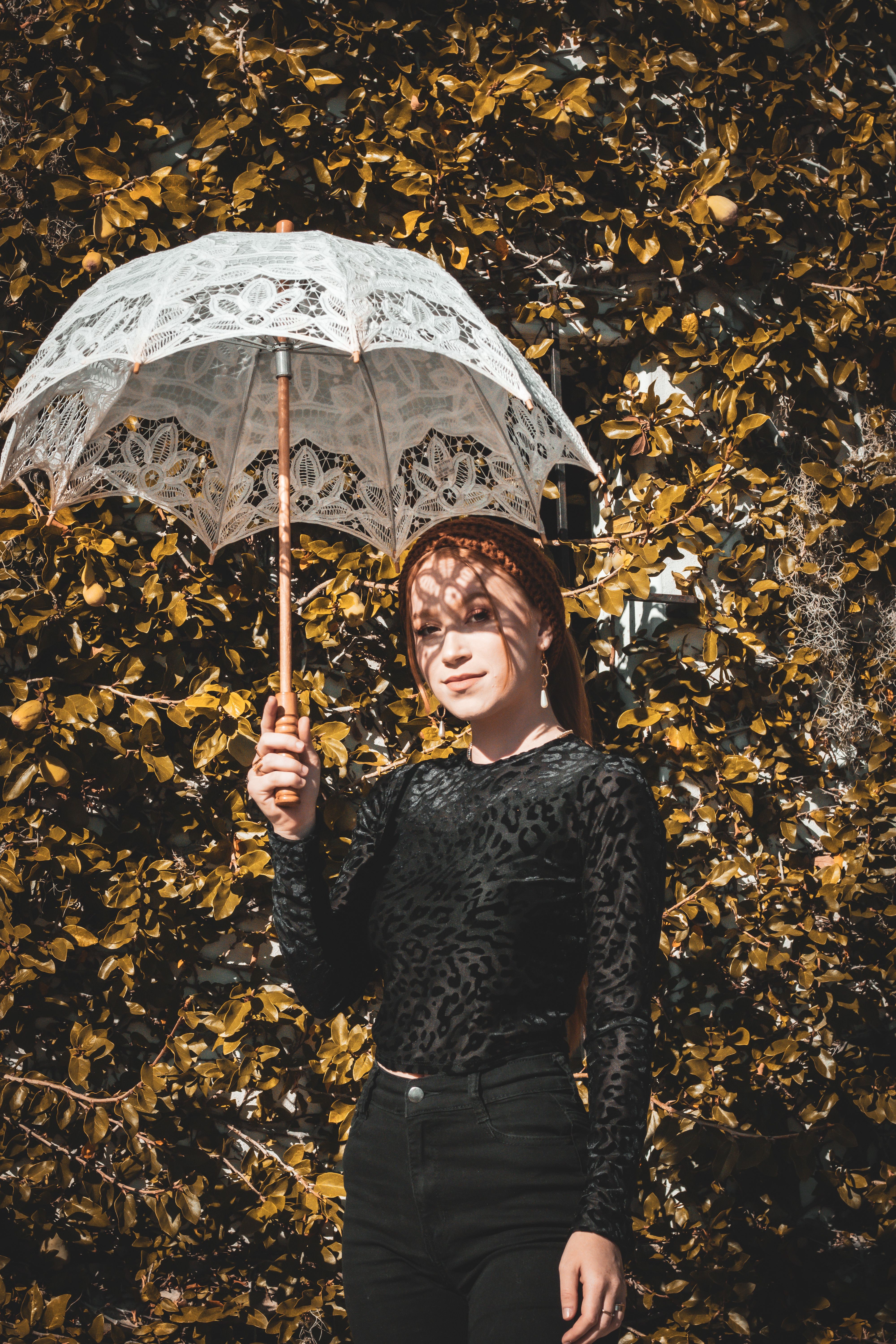 Woman Holding an Umbrella in Front of Vines · Free Stock Photo