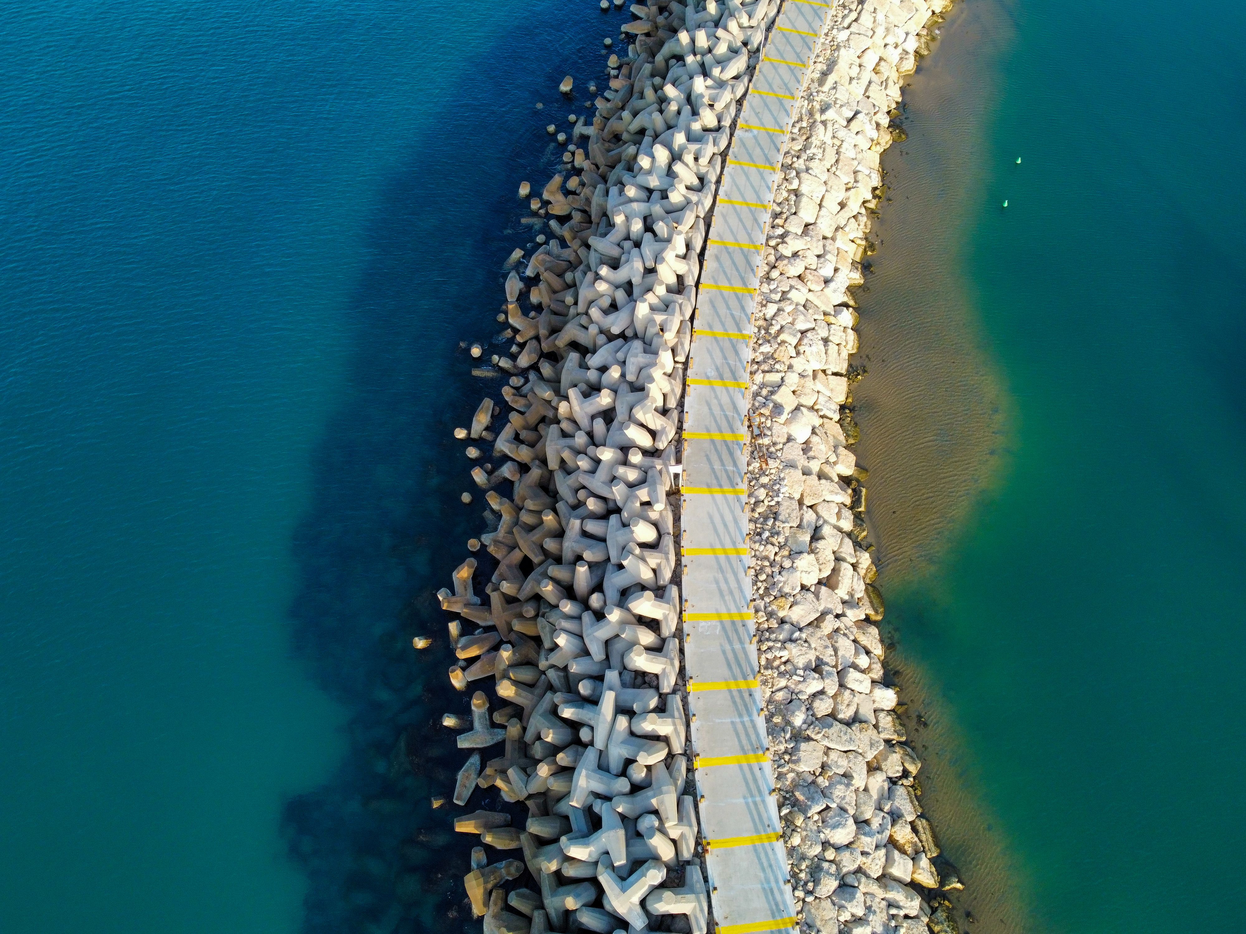 Curving walkway through concrete wave barriers beside blue water