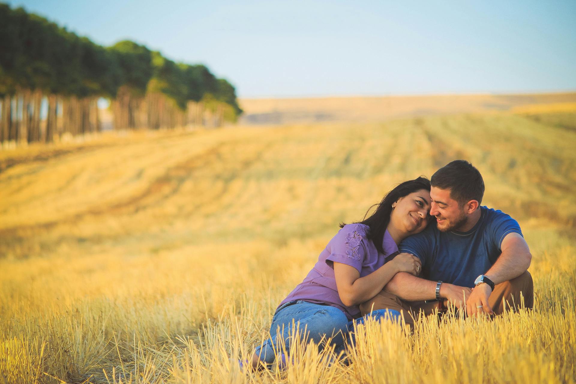 A loving couple enjoys a serene moment in a sunny field, symbolizing togetherness and happiness.